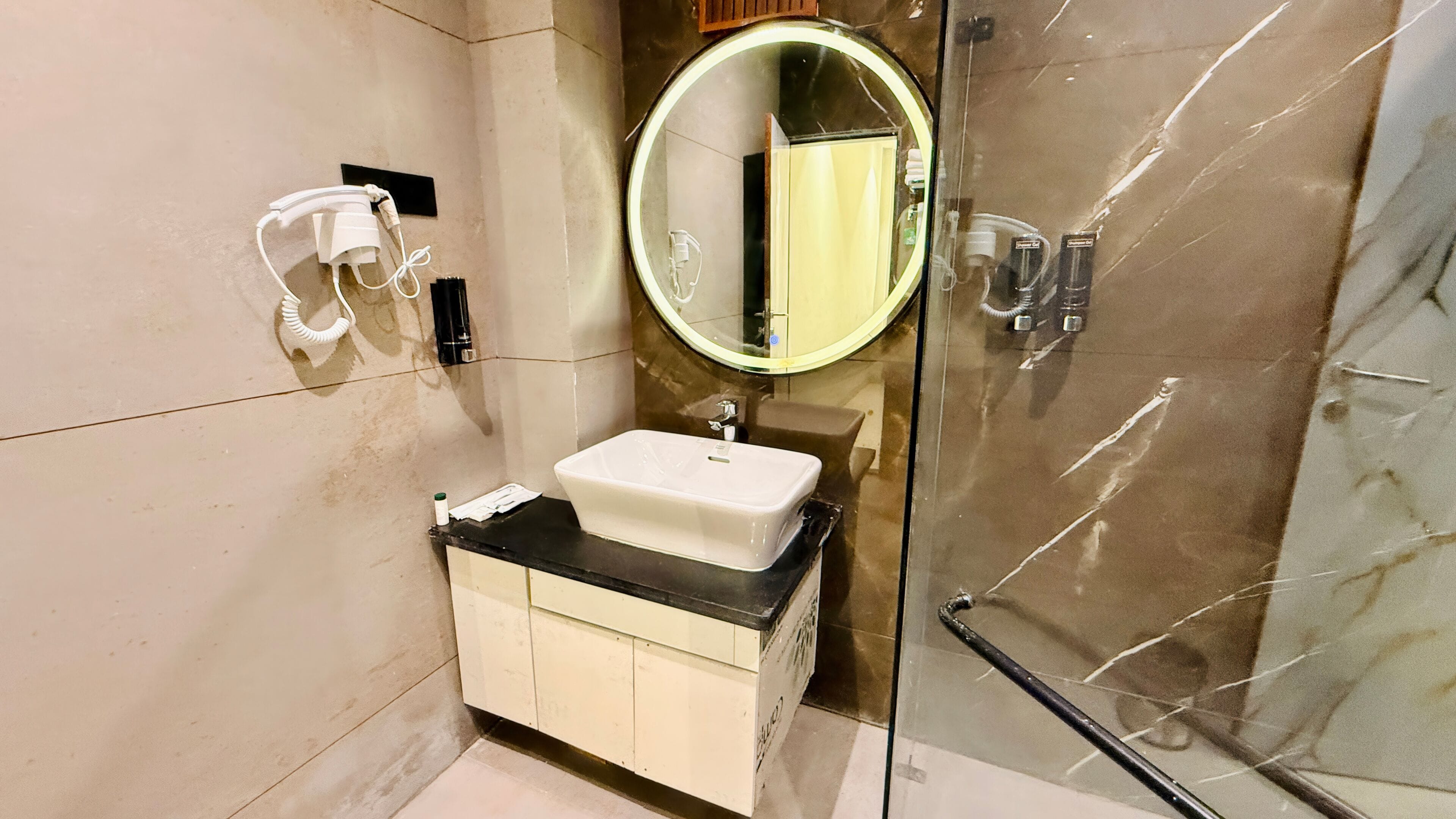 A modern bathroom with a glass shower enclosure, a white sink, and a round mirror.