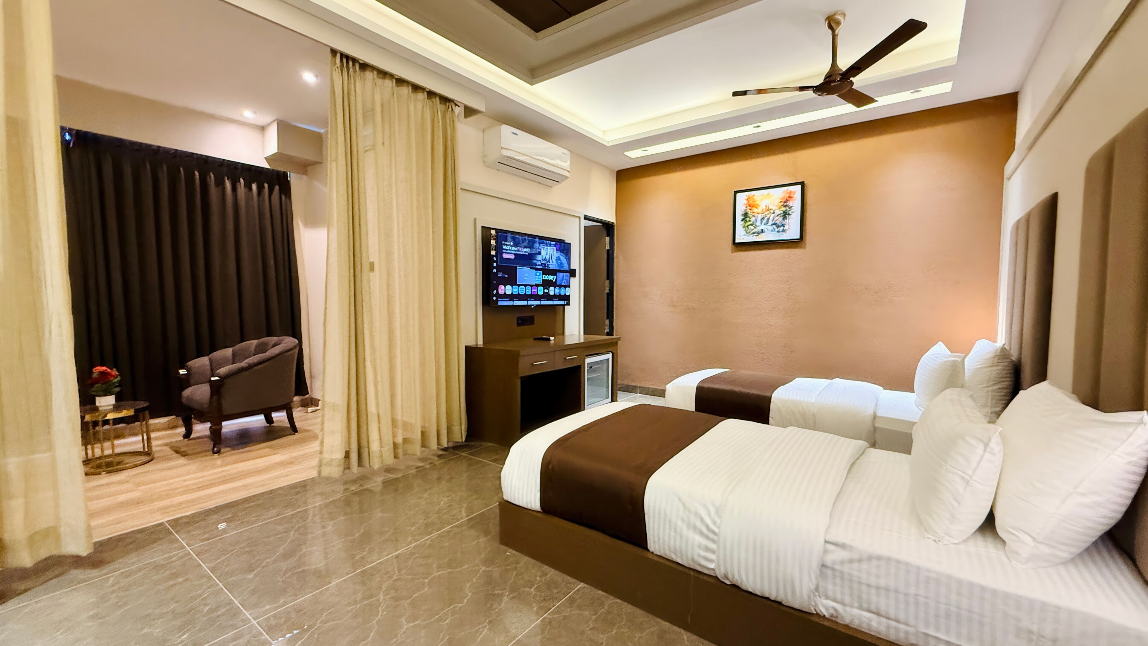 A hotel room with a bed, a desk with a television, a chair, and a ceiling fan.