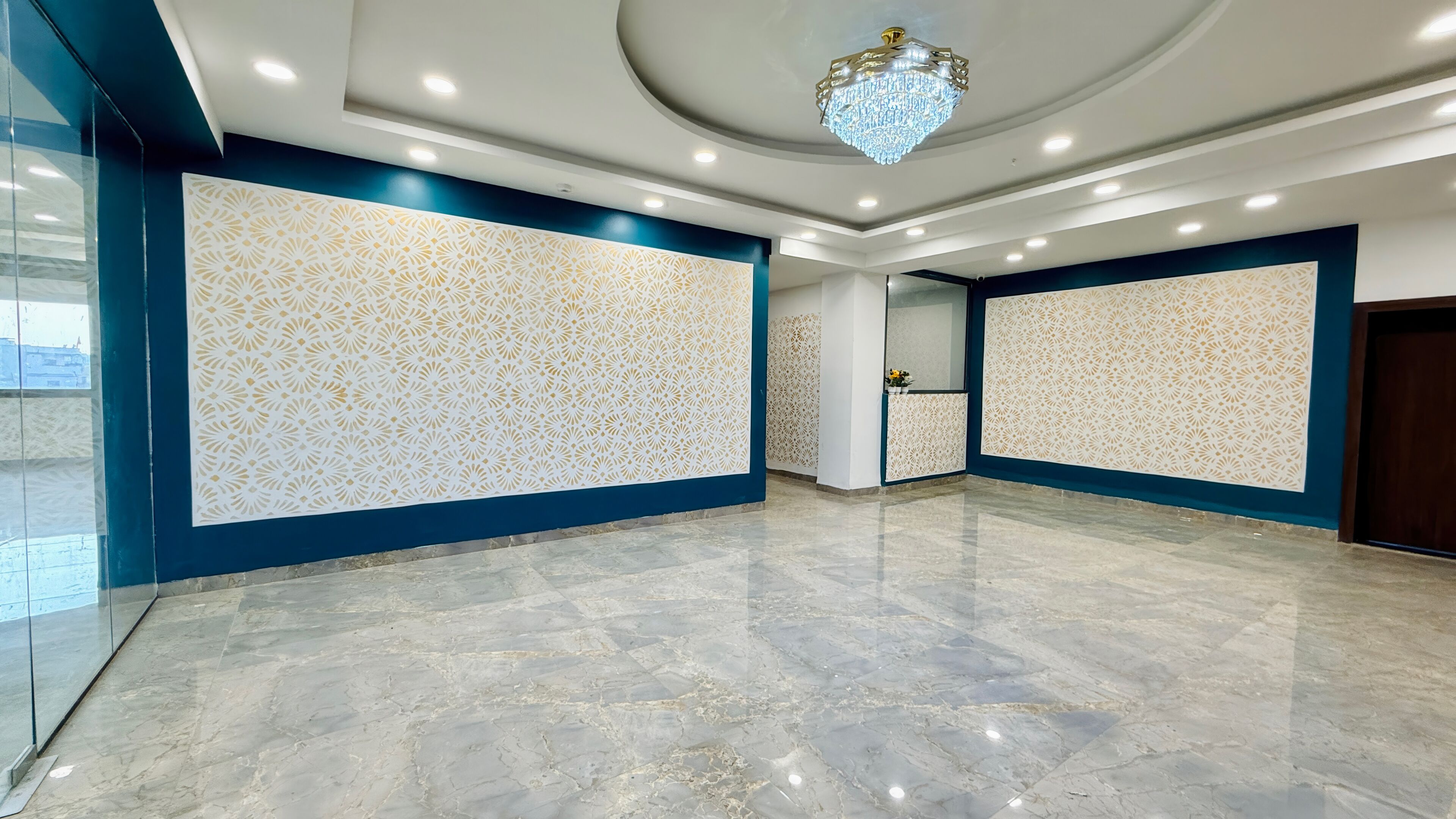 Una habitación amplia con suelo de mármol, paneles decorativos en la pared, iluminación empotrada y un candelabro.