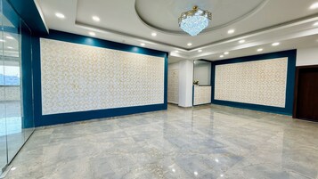 Una habitación amplia con suelo de mármol, paneles decorativos en la pared, iluminación empotrada y un candelabro.