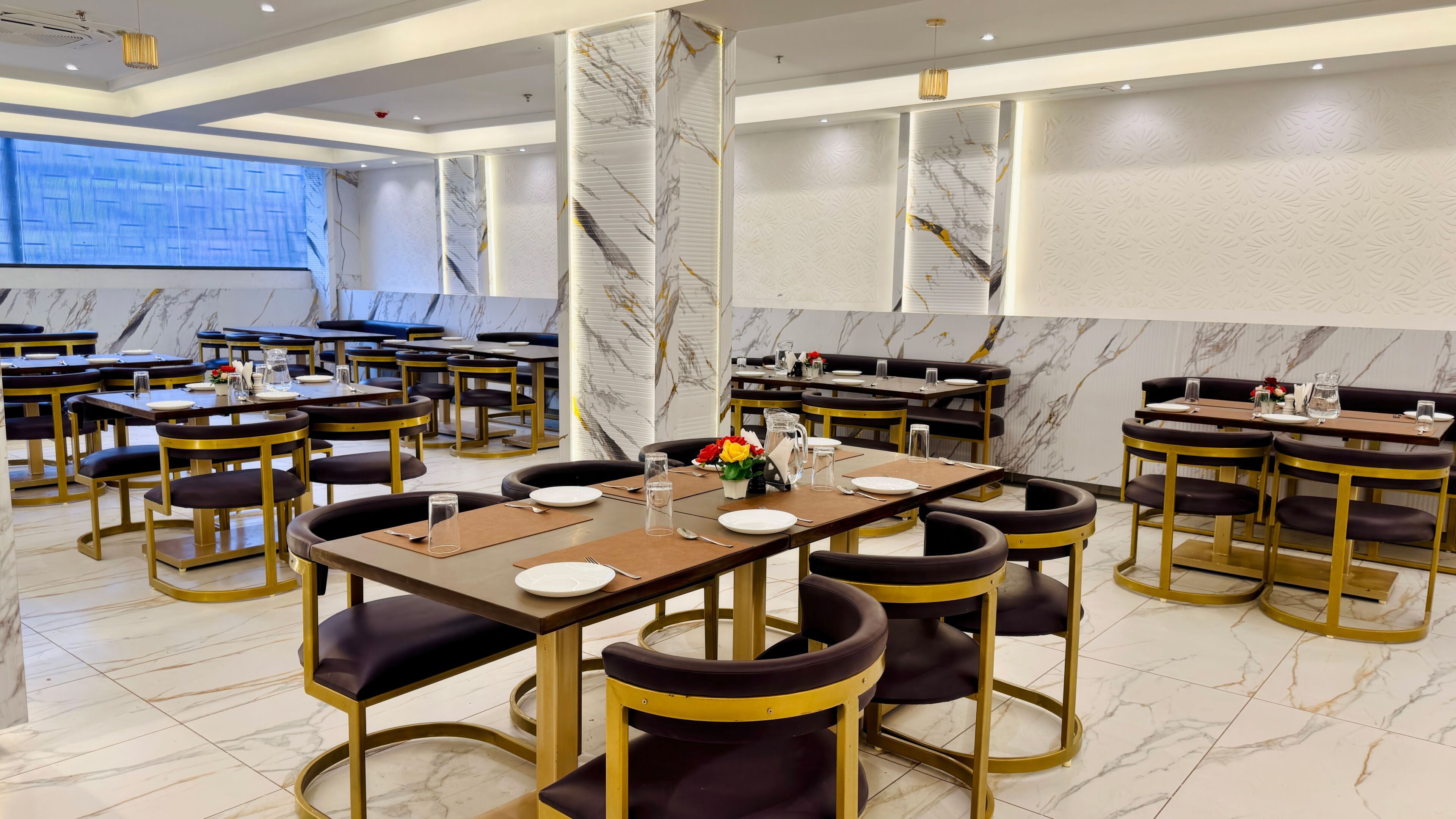 Um restaurante moderno com piso de mármore, mesas emolduradas a ouro e cadeiras estofadas em preto.