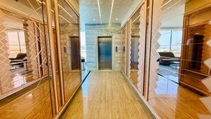 Un couloir moderne doté d’un ascenseur central, de cloisons en verre et d’un sol réfléchissant.