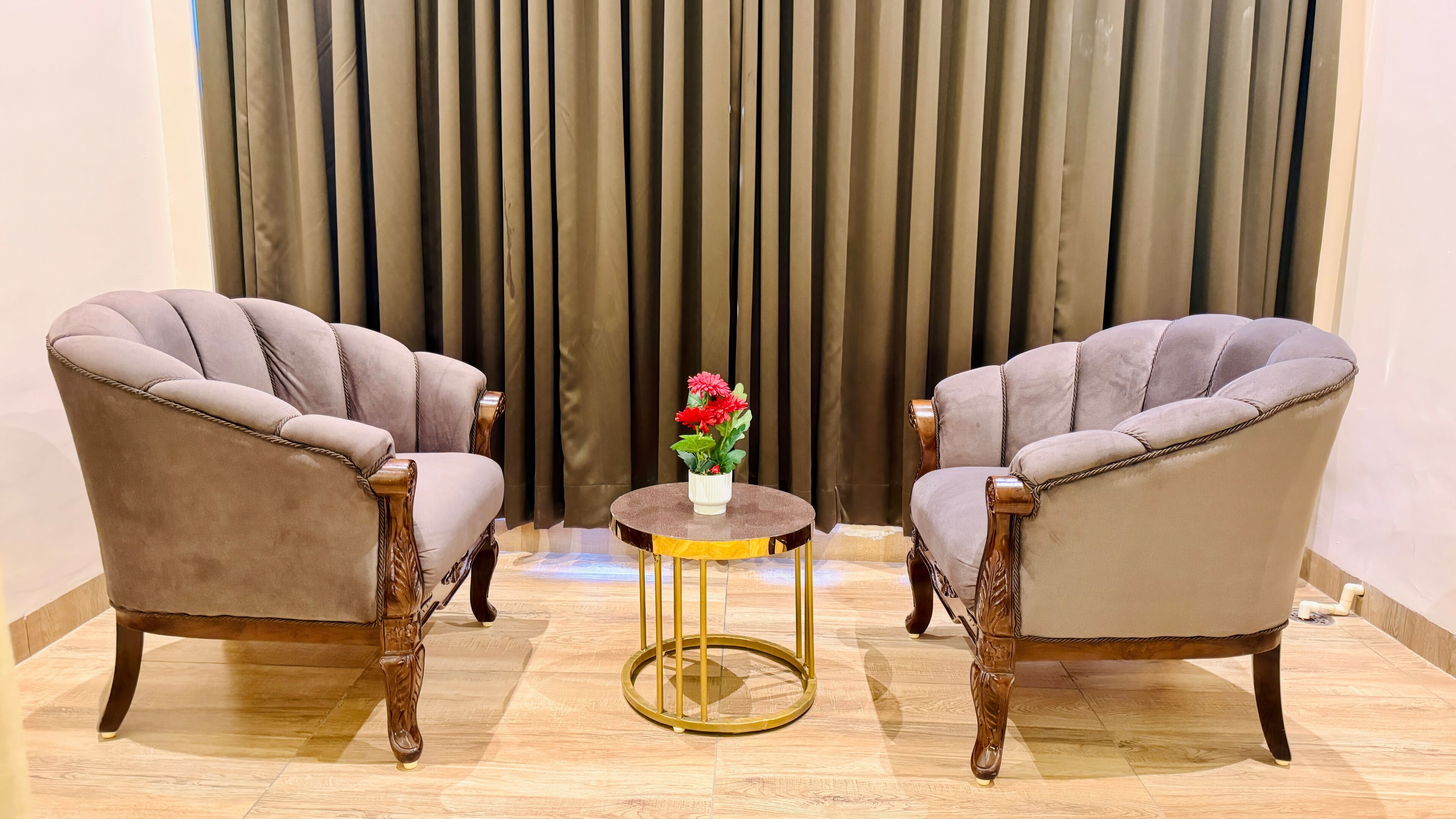 Two armchairs, a small round table with a vase of flowers, and a curtain backdrop.