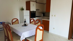 A dining area with a table set for two, a refrigerator, a stove, and a potted plant. - Cozy 2-bedroom apartment Near the Sea in Ika - with Terrace, AC & Free Parking (Ika)