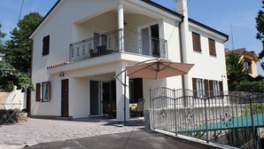 A two-story building with a balcony, a covered patio, and a gated entrance. - Cozy 2-bedroom apartment Near the Sea in Ika - with Terrace, AC & Free Parking (Ika)
