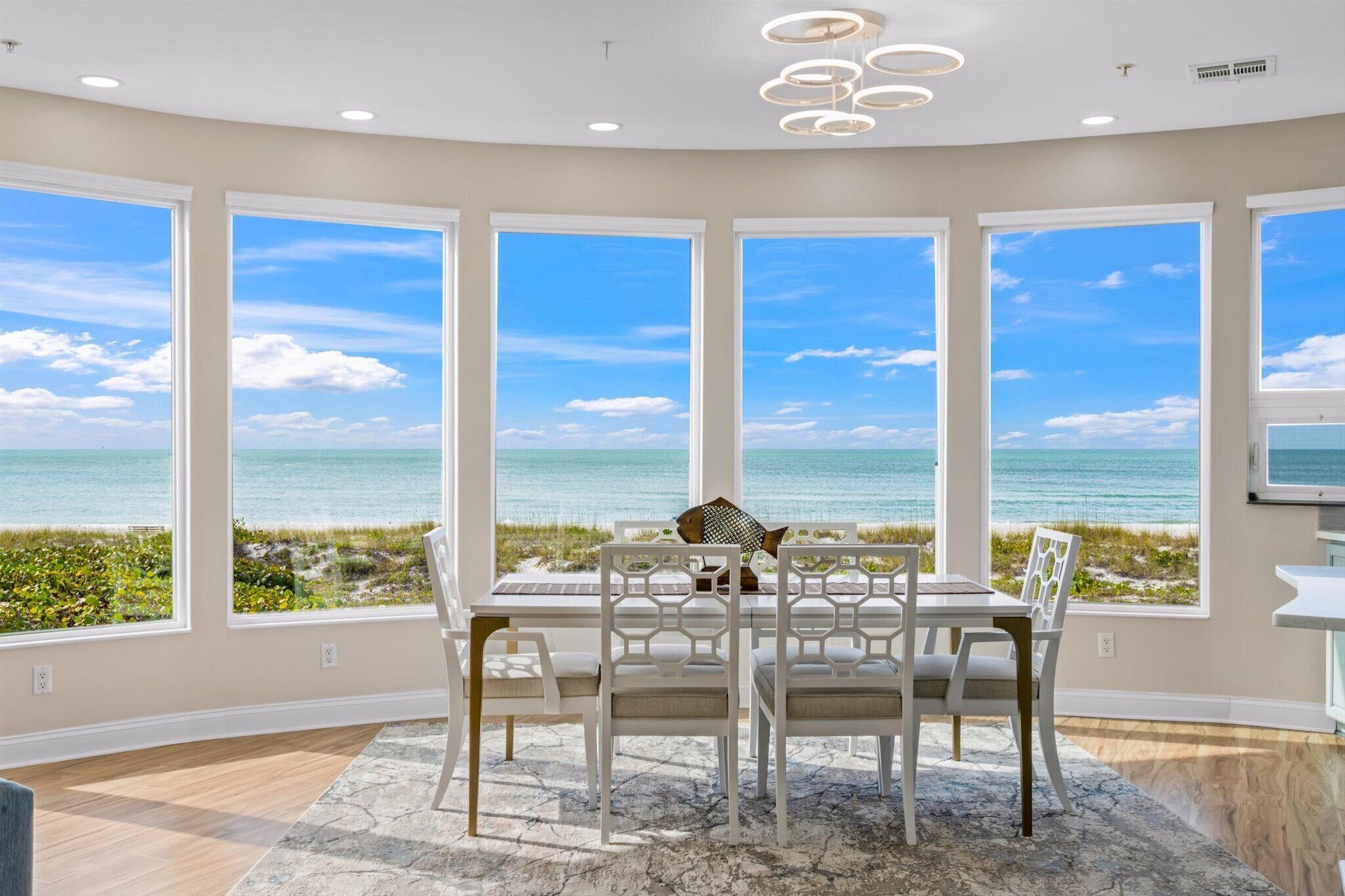 A dining area with a view of the ocean, large windows, and a ceiling light fixture.