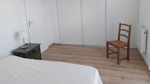 A bedroom with a bed, a wooden chair, a small table with a lamp, and a radiator. - DUPLEX house in a Landes village near the ocean (Lit-et-Mixe)