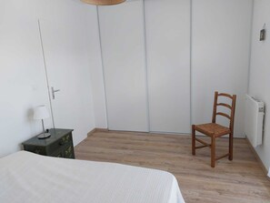 Ein Schlafzimmer mit einem Bett, einem Holzstuhl, einem kleinen Tisch mit Lampe und einer Heizung.