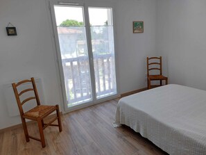Ein Zimmer mit einem Bett, zwei Holzstühlen, einem Fenster mit Blick und einem kleinen Bild an der Wand.
