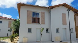 A modern building with a flat roof, white exterior walls, and wooden shutters on the windows. There are small windows and a door visible, and a street lamp is present. - DUPLEX house in a Landes village near the ocean (Lit-et-Mixe)