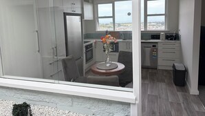 Una cocina moderna con refrigerador, horno y microondas. Cuenta con una zona de comedor con mesa y sillas, y una ventana con vistas a la ciudad.