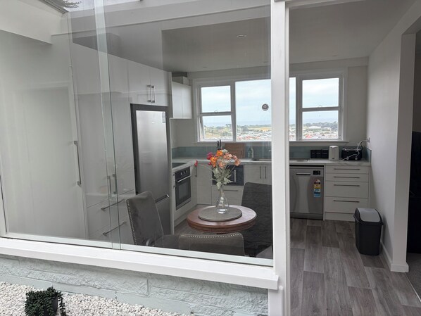 A modern kitchen with a refrigerator, oven, and microwave. There is a dining area with a table and chairs, and a window with a view of the city.