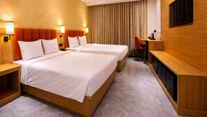 A hotel room with two beds, a desk, a TV, and a curtain. - Econostay (Bhilwara)