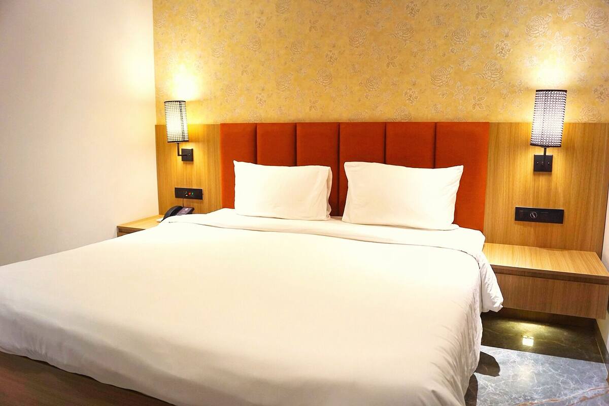 A hotel room with a large bed, two bedside tables, a wooden headboard, and wall-mounted lamps.