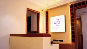 A reception area with a wooden reception desk, a wall-mounted sign with a logo, and a door with a wooden frame. - Econostay (Bhilwara)