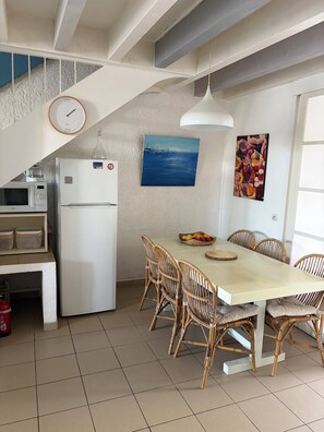 A kitchen with a dining table, chairs, a refrigerator, a microwave, a clock, and artwork on the walls.