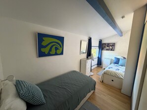 A bedroom with a bed, a dresser, a fan, and a window with curtains.