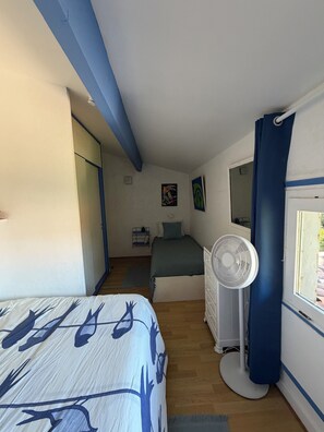 A bedroom with a bed, a dresser, a fan, and a window with curtains.
