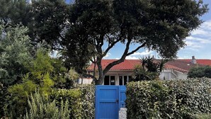 A pathway leading to a building with a red-tiled roof, surrounded by dense foliage and a blue gate. - Villa Olinka, behind the dune, plage des Bourdaines (Seignosse)