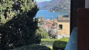 Vista de un lago con montañas al fondo, un edificio de fachada amarilla y abundante vegetación.