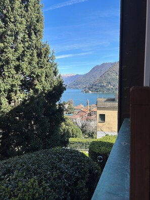 A view of a lake with mountains in the background, a building with a yellow facade, and dense greenery. - Amazing studio appartment, newly renoveted, walking distance to Como. (Como)