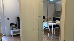 Un pasillo con un armario espejado, un banco blanco con un marco de fotos y una vista de un comedor con mesa y sillas.