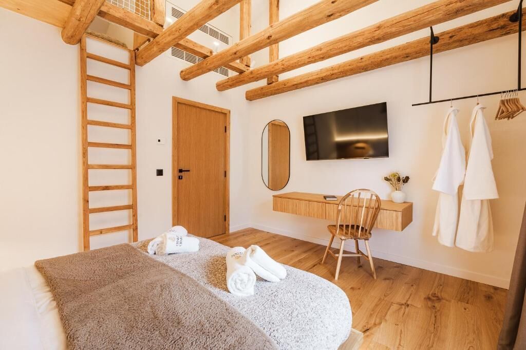 A bedroom with a bed, a wooden ladder, a desk, a chair, a TV, and a mirror.
