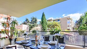 Un espacio de comedor al aire libre con una mesa para dos, plantas en macetas y vistas a edificios y árboles.