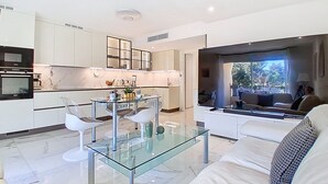 Una cocina moderna con armarios blancos, una mesa de comedor de vidrio y una zona de estar con sofá y sillas.