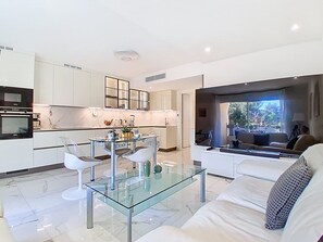 Eine moderne Küche mit weißen Schränken, einem Glastisch und einer Sitzecke inklusive Sofa und Stühlen.