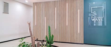 Een receptiegedeelte met een wand van houten latten, een cactussplant en een bord met de tekst 'BLUE WAVE'.
