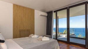 Camera d'albergo con un letto, parete in legno, condizionatore, balcone con vista sul mare e un'ampia porta finestra.