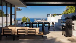 Una veranda esterna con un divano, sedie, un barbecue e vista sull'oceano.