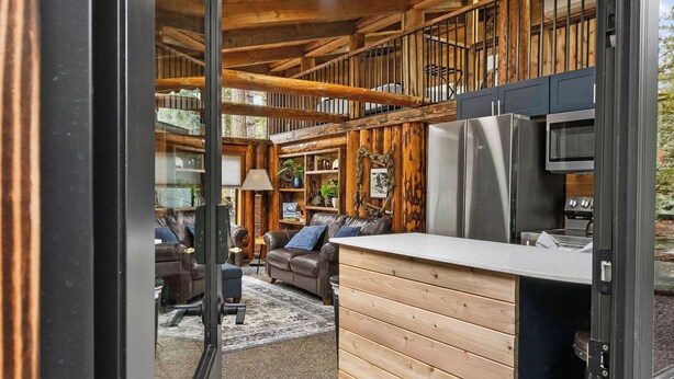 A spacious interior with a wooden ceiling, a kitchen area, and a seating area with sofas and a rug. - Unique Log cabin @ Rainier with Hot Tub-Fast WiFi (Ashford)