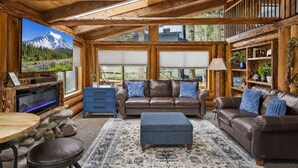 A log cabin interior with a fireplace, leather sofas, a television, and a bookshelf. - Unique Log cabin @ Rainier with Hot Tub-Fast WiFi (Ashford)