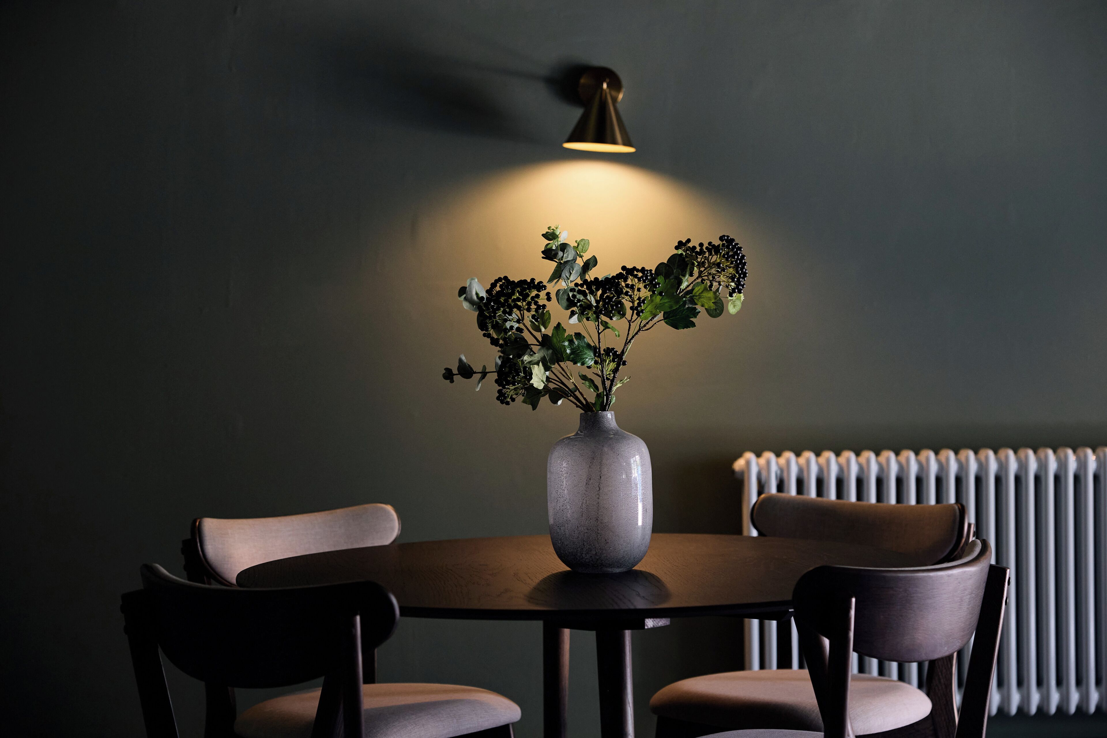 A dining table with a vase of flowers, two chairs, and a wall-mounted light fixture.