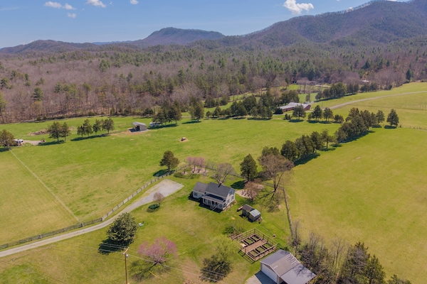 A scenic farmhouse nestled within expansive, fenced pastures and surrounded by rolling mountain vistas.