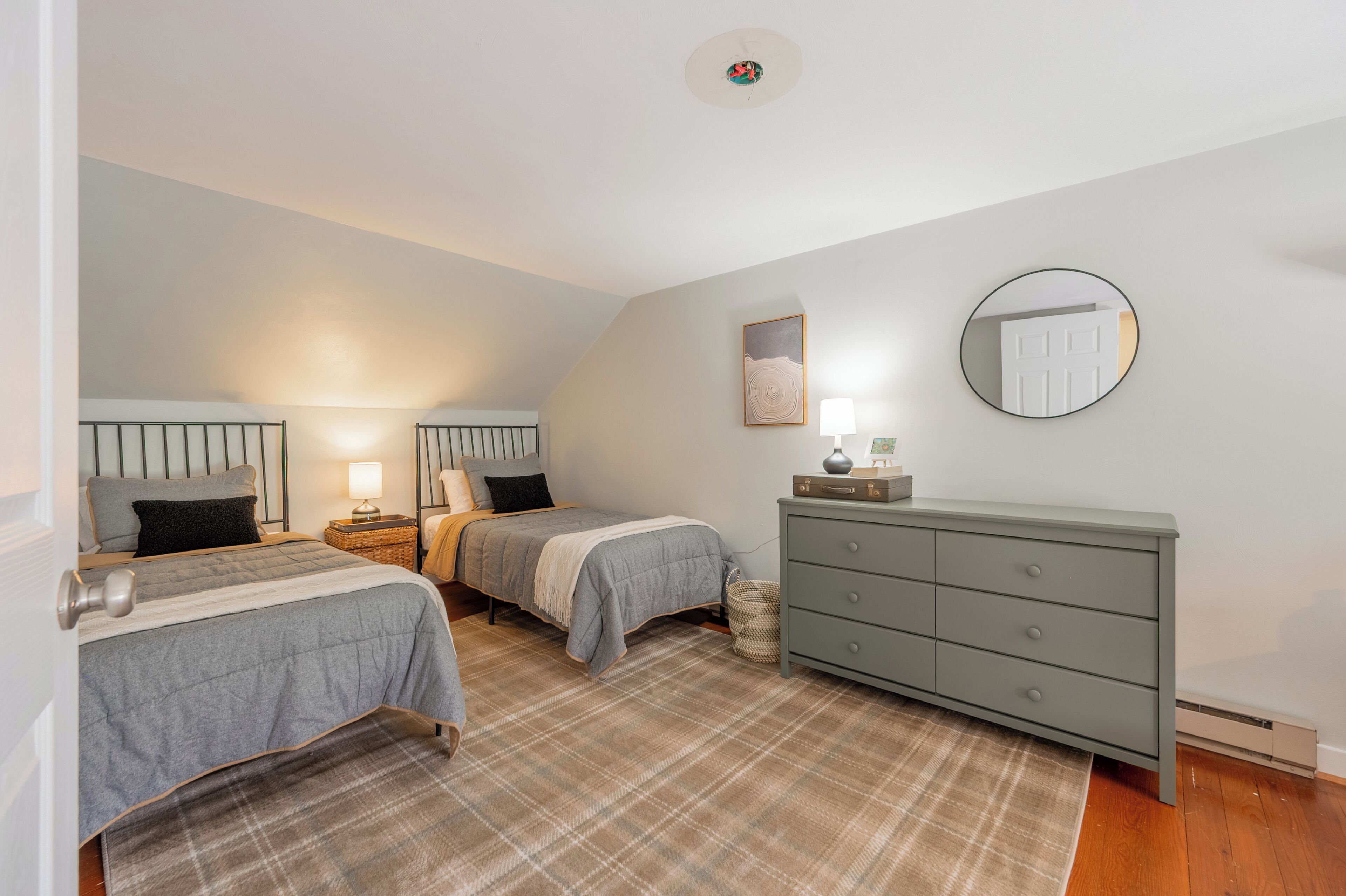 A bedroom with two beds, a dresser, a mirror, and a ceiling light.
