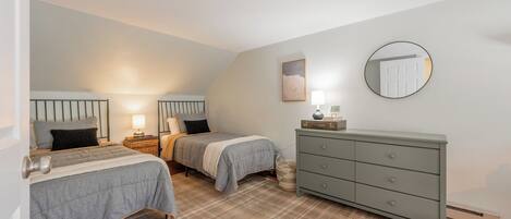 A bedroom with two beds, a dresser, a mirror, and a ceiling light.