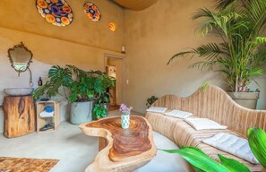 Ein Zimmer mit einem gewebten Sofa, einem Holztisch und großen Topfpflanzen.