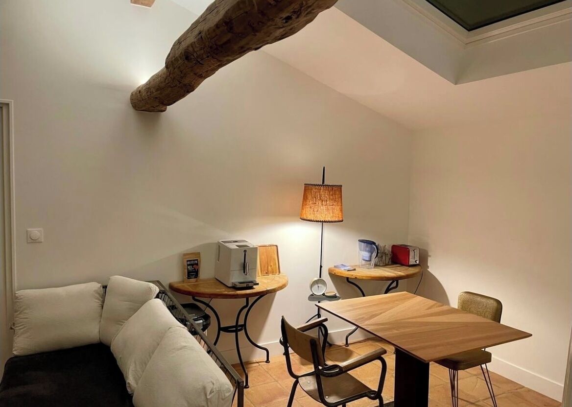 Une pièce de taille modeste, comprenant un canapé, une table à manger, une lampe et un plafond avec une poutre en bois.