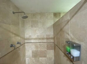 A shower area with a handheld showerhead, a glass partition, and a soap dispenser. - ANGEL OF INDEPENDENCE (Ciudad de México)