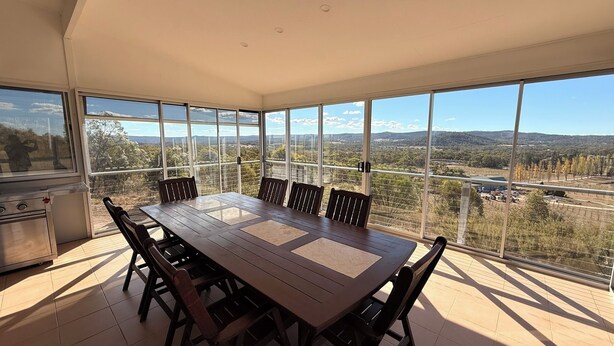 A dining area with a large table and chairs, large windows with a view of a landscape, and a kitchen area with a stove.