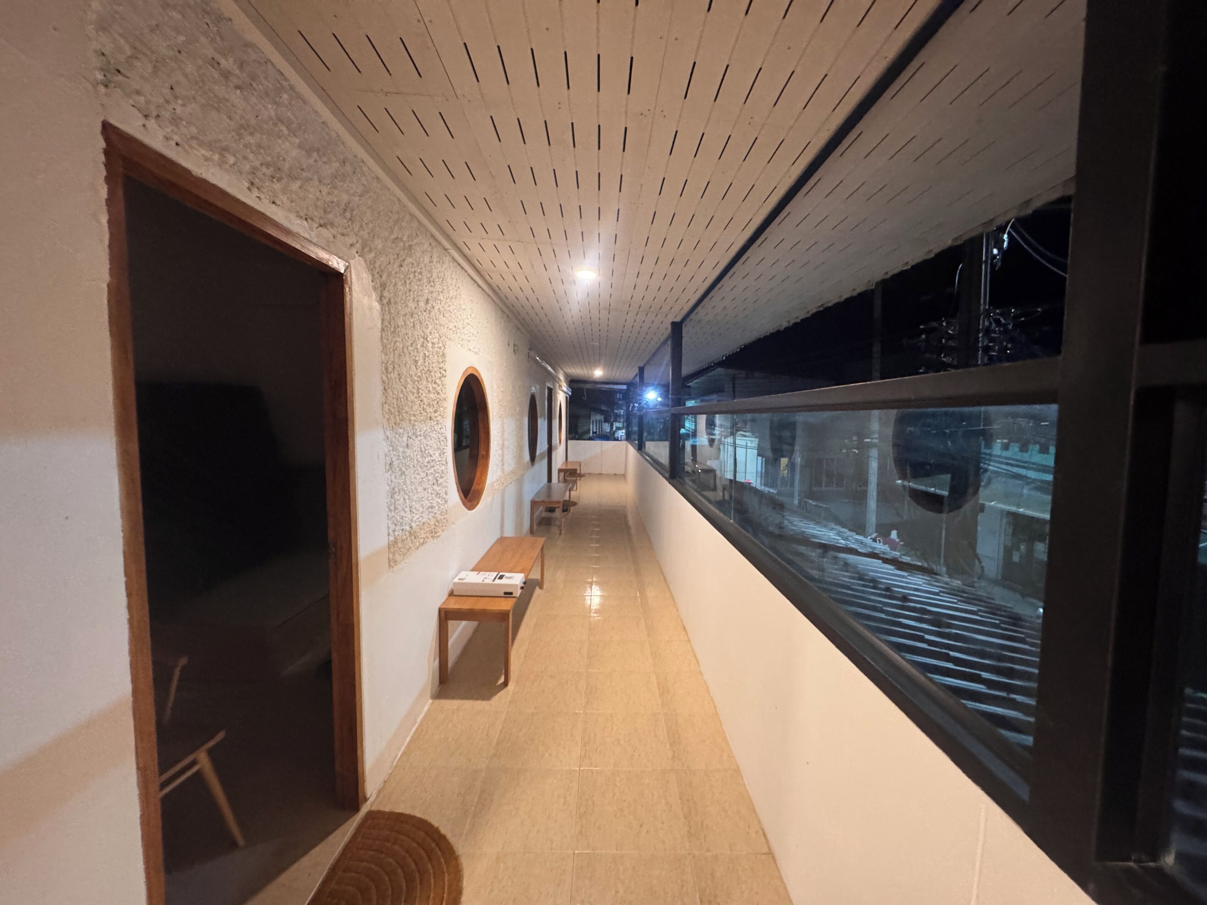 A corridor with a tiled floor, wooden benches, circular wall decorations, and a view through a glass window.