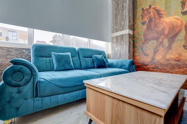 Un canapé bleu avec une table en marbre, dans une pièce où est accroché un grand tableau représentant un cheval.