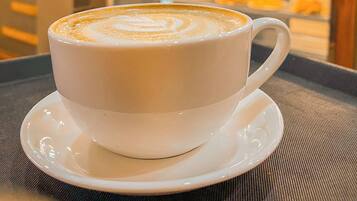 A cup of coffee with latte art on a saucer, placed on a table in a cafe with hanging lights and a counter in the background.