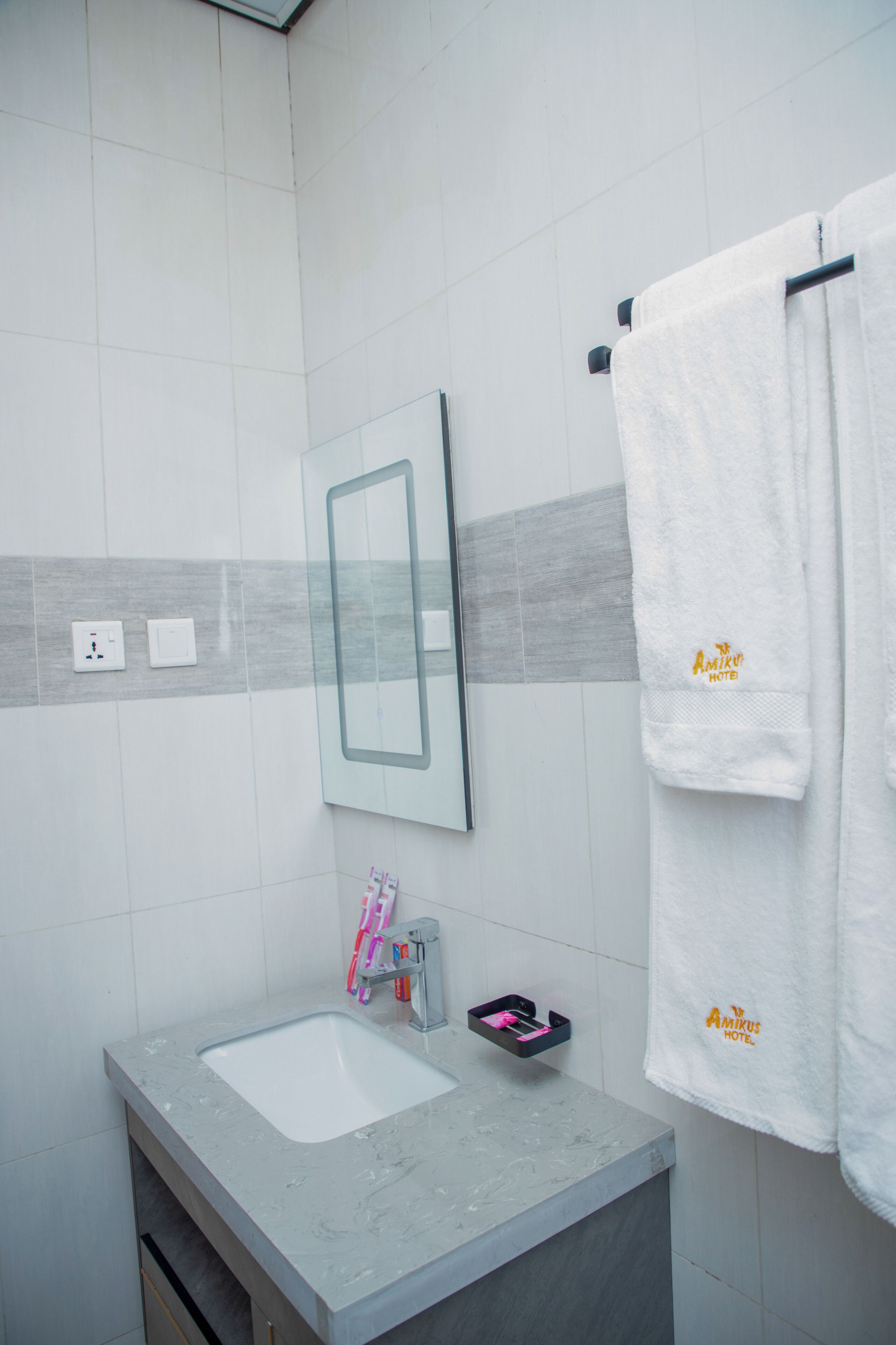 A bathroom with a marble sink, a mirror, a towel rack with a white towel, and a small shelf with toiletries.