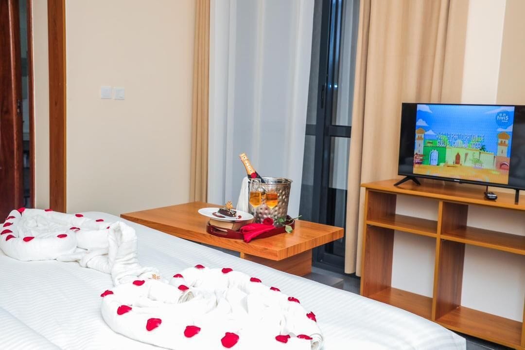 Een hotelkamer met een bed, nachtkastje met een flesje, een afstandsbediening en een televisie.