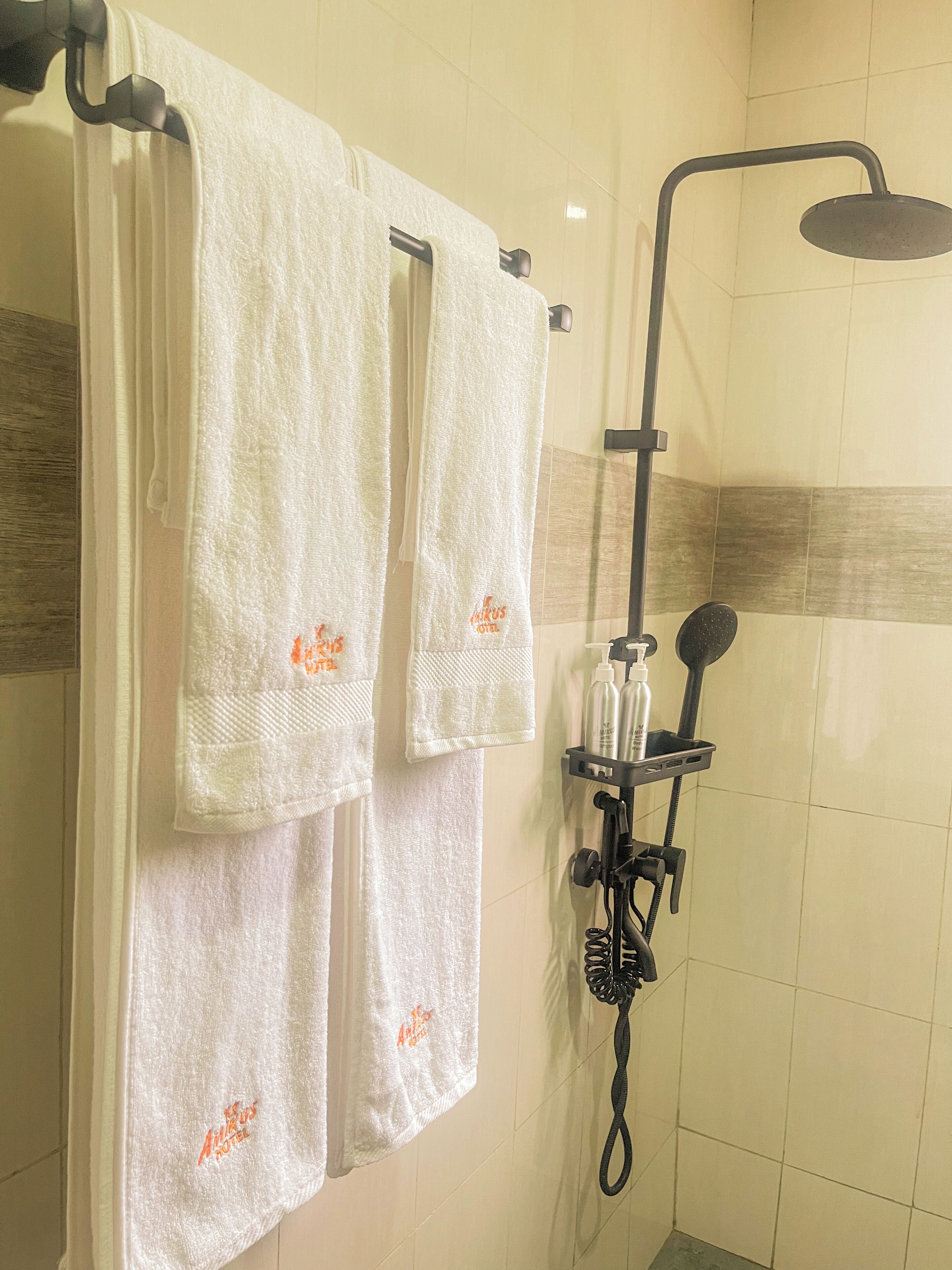 A shower area with a handheld showerhead, a towel rack with three white towels, and a soap dispenser.