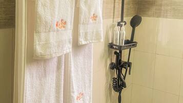 A shower area with a handheld showerhead, a towel rack with three white towels, and a soap dispenser.